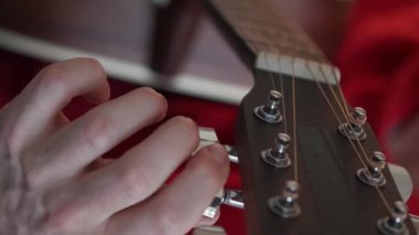 Vertical video. Guitar tuning. Male hobby. Instrumental skill. Closeup man adjusting pegs and gears on string with headstock light room interior blur.