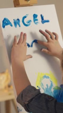 Vertical video. Finger painting. Kid art. Little artist imagination. Talented girl hands creating blue yellow color angel heart artwork on easel.