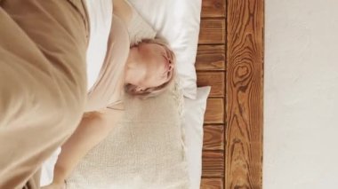 Vertical video. Bad morning. Angry woman. Uncomfortable sleep. Displeased lady spinning on inconvenient bed impossible to rest light home interior.