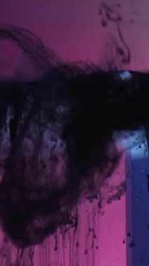 Vertical video. Ink drop. Paint drip. Smoke flow. Black fluid motion on pink blue color neon light glass cube edge in water on dark grunge abstract background.