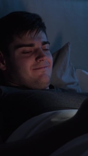 온라인 잠자리 미디어 호기심많은 남자가 침대에서 스마트폰으로 스크롤 피드를 즐기고 — 비디오