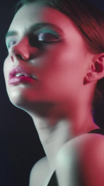 垂直录像 90年代时尚 霓虹灯的美丽复古派对的样子 淡出的少女模特儿的脸 有着艺术的妆容 闭着眼睛 闪烁着深紫蓝色的光芒 在黑色上跳舞 — 图库视频影像