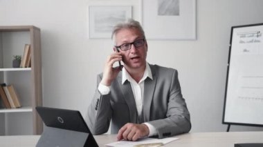 Phone interview. Business counselling. Professional advice. Confident cheerful senior executive man in suit glasses talking at light modern office interior.