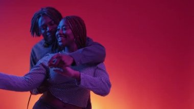 Dancing couple. Enjoying time. Neon light portrait. Positive smiling black man and woman moving on music together on red blue background slow motion.