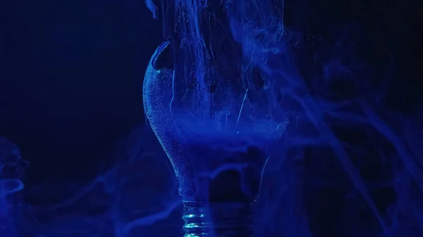 Lamp explosion smoke cloud. Power failure. Defocused blue color vapor haze in broken glass light bulb on dark night abstract background.