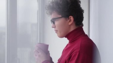 Good morning. Curious man. New day inspiration. Relaxed casual guy with cup hot coffee looking window with interest in light room interior.