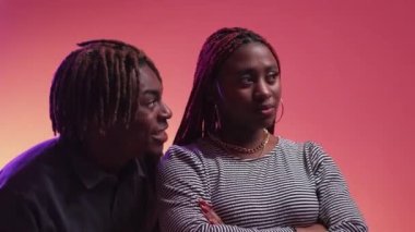 Supportive relationship. Beloved couple. Neon light portrait. Funny black man tickling sad woman for cheer up posing purple peach pink background.