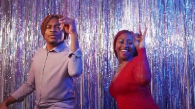 Party excitement. Satisfied couple. Holiday joy. Happy black man and woman impressed of celebration showing ok gesture on cascade curtain background slow motion.