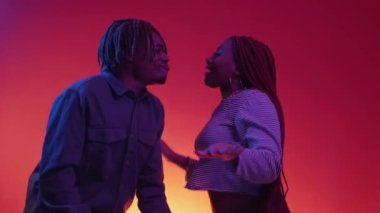 Dancing couple. Happy relationship. Neon light portrait. Positive smiling black man and woman having fun moving on red blue background.