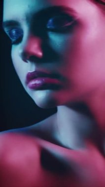 Vertical video. 90s beauty. Neon face. Disco fashion look. Closeup of relaxed teen girl model with artistic makeup closed eyes posing in red purple blue color flash light on dark.