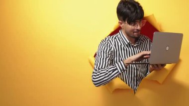 Digital people. Electronic nerd. Information technology. Happy geek man enjoying using laptop in orange breakthrough torn paper hole copy space background.