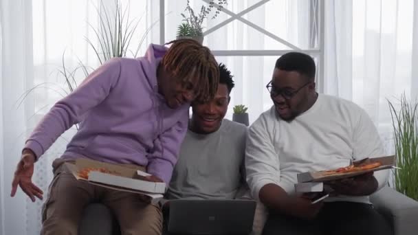 在线会议 黑人男子 回家吃晚饭 笔记本电脑照明室内虚拟会议期间 快乐的男性朋友们正在吃披萨 — 图库视频影像