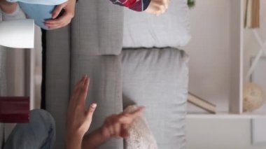 Vertical video. Meeting friends. Diverse couple. Enjoying fun. Happy casual man and woman playing game rock-paper-scissors sitting light room interior.