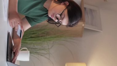 Vertical video. Online banking. Internet payment. Electronic transaction. Smart woman using laptop paying with credit card transferring money at home workplace.