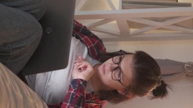 Vertical video. Remote job. Freelancer lifestyle. Digital business. Serious smart woman working from home online using laptop on couch.
