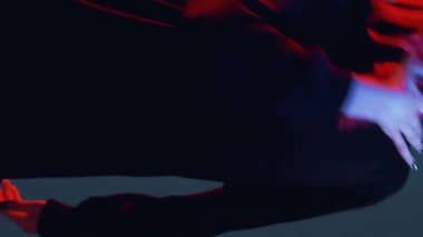 Vertical video. Hip hop dance. Rap music fan. Night party. Neon light girl in black hoodie performing freestyle movements red blue color glow on dark.