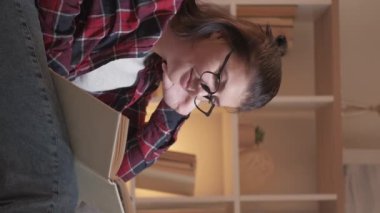 Vertical video. Reading hobby. Lazy weekend. Evening home leisure. Curious smiling woman enjoying rest with funny book story on cozy couch in living room.