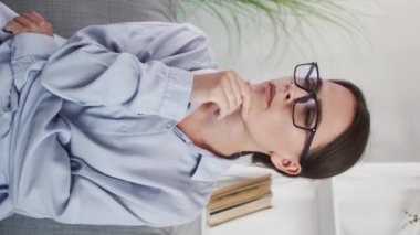 Vertical video. Business contemplation. Corporate webinar. Remote learning. Pensive puzzled smart intelligent woman in glasses listening nodding at home virtual class.