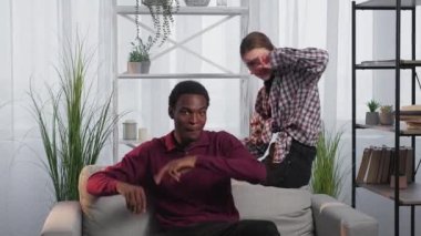 Home leisure. Diverse couple. Happy relationship. Positive funny black man and european woman having fun sitting sofa in light room interior slow motion.