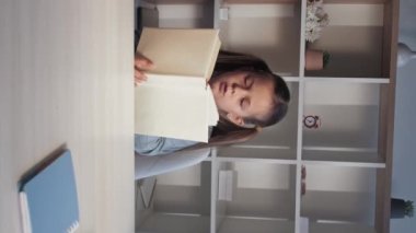 Vertical video. Kid reading. Children education. Home learning. Motivated intelligent little girl studying with open book at workplace.