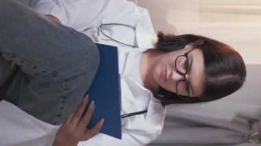 Vertical video. Doctor report. Medical paperwork. Professional career. Woman practitioner working filling healthcare insurance writing prescription form on clipboard at clinic.
