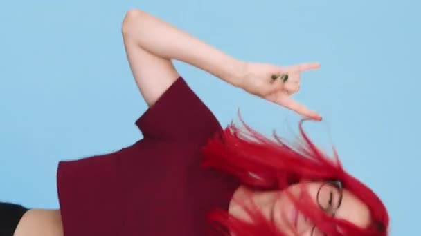垂直ビデオ ロックジェスチャー ヘビーメタルファン 肯定的なライフスタイル 興奮した幸せなパンク女の子とともに赤い髪楽しいです音楽ダンスとともに角で青の背景シームレスなループ — ストック動画