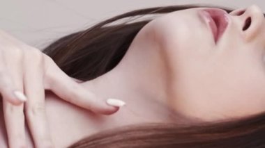 Vertical video. Skincare beauty. Sensual woman. Smooth treatment. Graceful beautiful brunette lady tenderly touching neck decollete light blur slow motion.