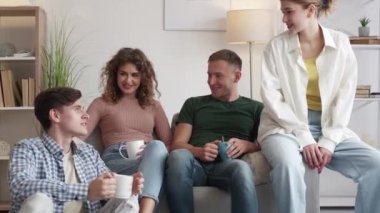 Double date. Happy couple. Home meeting. Relaxed male and female friends talking and drinking coffee sitting together on sofa light room interior.