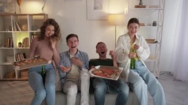 Watching sport. Competitive mood. Friends meeting. Shocked men feeling relief looking TV together with women with pizza in light home interior.