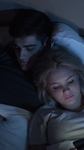 小夜叉 网络休闲 通讯问题 厌倦了厌倦了的夫妇使用手机打电话一起躺在床上 垂直录像 — 图库视频影像