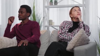 Love unity. Diverse couple. Romantic affection. Embarrassed black man and european woman putting hands each other sitting sofa in light room interior.