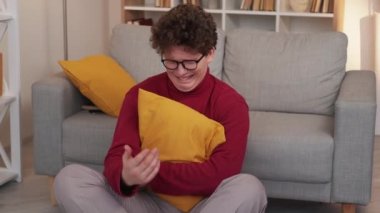 Unfair situation. Desperate man. Depressed feelings. Sad gloomy guy crying sitting floor grasping cushion in light room interior.