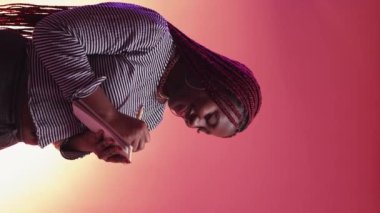 Vertical video. Romantic letter. Inspired woman. Neon light portrait. Happy black lady writing in notepad on purple peach pink background.