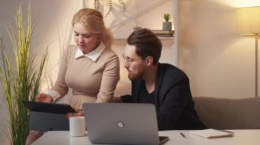 Business project. Office colleagues. Teamwork discussion. Inspired man and woman looking tablet computer sitting in light room interior.