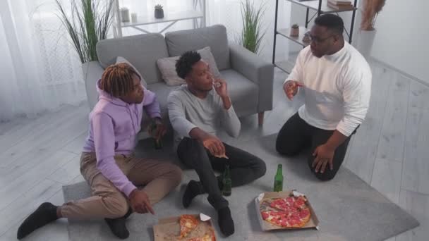 友好的讨论 家庭会议 有灵感的黑人男人放松的嬉皮士与啤酒和比萨饼一起聊天 坐在地板上 室内灯光明亮 — 图库视频影像