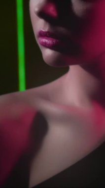 Vertical video. 90s beauty. Fashion model. 2000s look. Cropped portrait of teen girl face posing in red green color neon flash light on black.