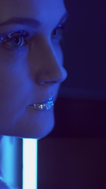垂直ビデオ キラキラしたメイク ネオンの女の子 ナイトクラブのファッション 青い紫色のフラッシュライト女性顔で輝く金属アイシャドウ唇でミラーオンダーク — ストック動画