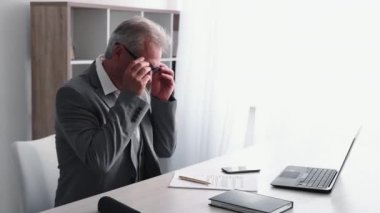 Senior career. Paperwork process. Professional occupation. Confident smart senior business man wearing glasses signing papers at light office workplace interior with free space.