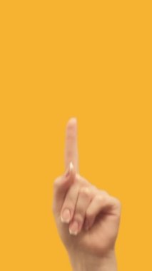 Vertical video. Attention gesture. Information here. Female hand recommending finger pointing up at yellow empty space promotional background.