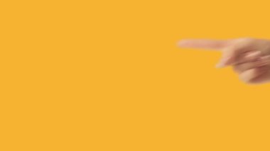 Attention gesture. Recommending sign. Female hand finger pointing left at something invisible on orange empty space advertising background loop.