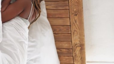 Vertical video. Morning awakening. Happy weekend. New day beginning. Relaxed smiling woman waking up stretching in bed in light home bedroom interior.