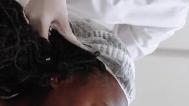 Vertical video. Beauty procedure. Female patient. Skincare cosmetology. Unrecognizable dermatologist putting medical hat on happy woman in clinic.