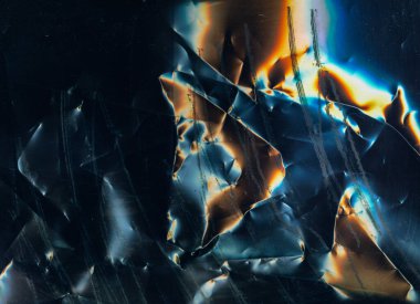 Scratched film texture. Crumpled noise. Distressed foil surface. Orange blue white color glow dust stains on dark black grunge abstract background.