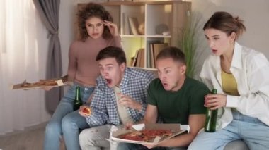 Competitive mood. TV translation. Home party. Shocked male and female friends meeting for watching video eating pizza in light room interior.