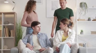 Unexpected meeting. Happy friends. Home leisure. Smiling couple making surprise coming to male and female sitting sofa in light room interior.