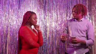 Budget spending. Couple relationship. Party celebration. Tricky woman taking over cash dollars in miserly black man posing shimmering cascade curtain background.