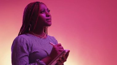 Diary notes. Romantic woman. Neon light portrait. Inspired black lady writing thoughts in notepad on purple peach pink background copy space.