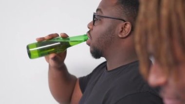 Refreshing beer. Friendly meeting. Advertising product. Relaxed hipster black men drinking alcohol from bottles posing on light background.