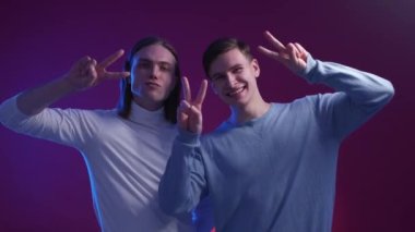 Peace gesture. Excited men. Neon light portrait. Expressive positive guys showing two fingers posing blue violet background.