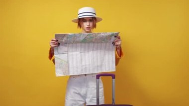 New country. Lost woman. Journey destination. Concentrated pretty lady looking confused choosing correct way on map posing with suitcase on yellow background.